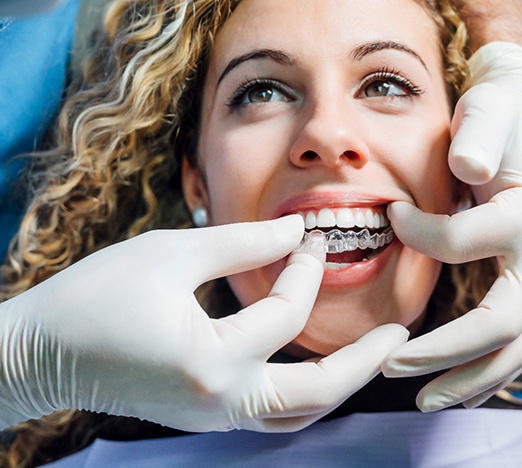 Orthodontist with white gloves placing Invisalign aligners on patient's teeth