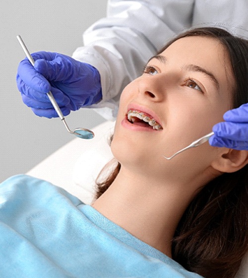 A dentist performing a checkup on a female patient who is wearing braces