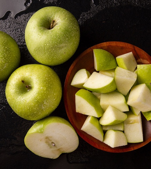 An image of three whole apples and a bowl of diced apples