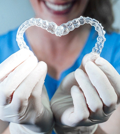 A dental professional holds two Invisalign aligners in their hands to create a heart