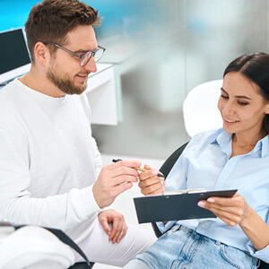 orhtodontist handing woman a pen to fill our financial forms on a clipboard