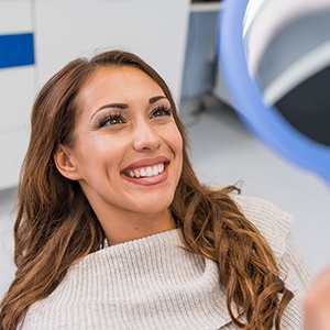 Woman smiling at reflection in handheld mirror