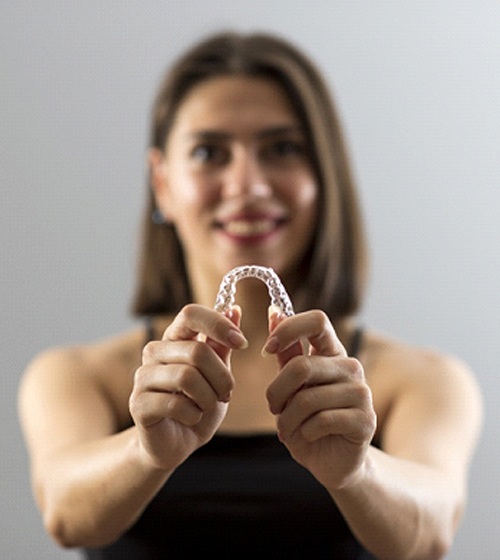 A young female holding a clear aligner in her hands after learning about the cost of Invisalign in Plano