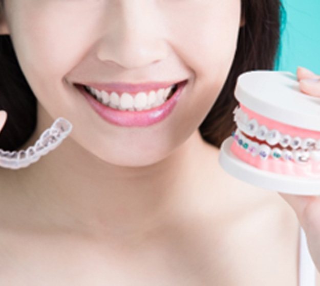 Smiling woman holding Invisalign in one hand and braces in the other