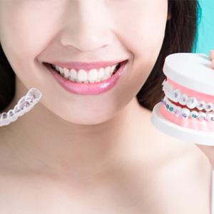 Woman holding Invisalign clear aligner and model with traditional braces