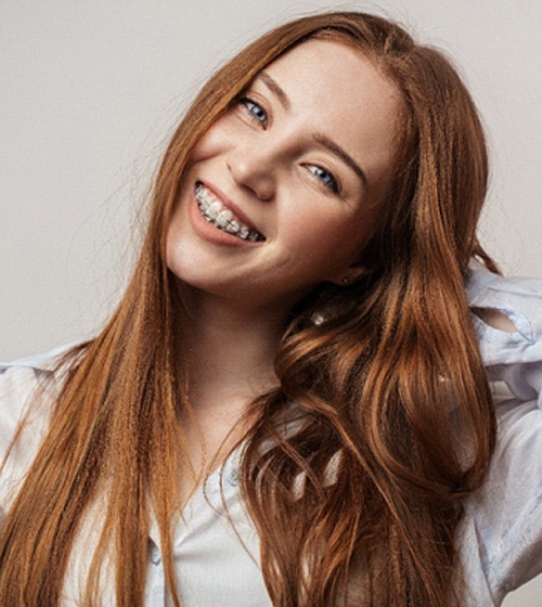 A young girl with long, red hair, smiling and showing off her metal fixtures after having a loose braces bracket in Plano fixed