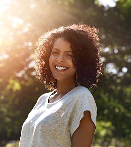 A woman wearing a gray t-shirt and smiling after seeing her orthodontist in Plano for orthodontic treatment