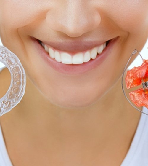 Woman smiling as she holds two orthodontic retainers