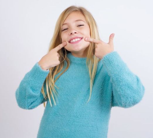 Happy young girl pointing at her teeth