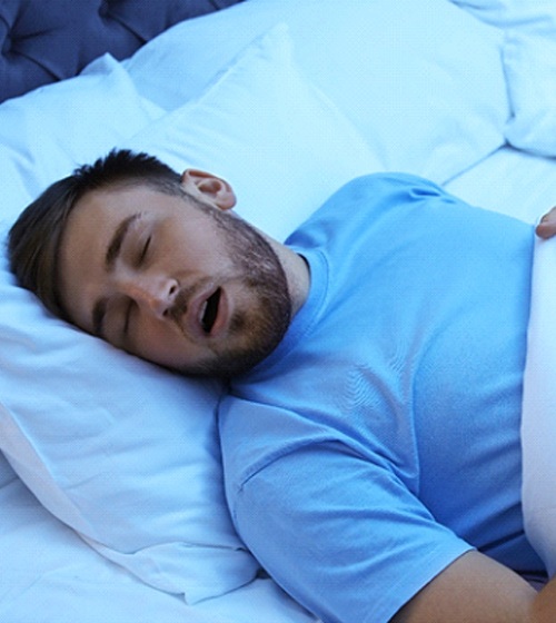 A young man asleep in bed with his mouth open and snoring
