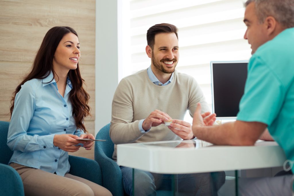 Smiling couple talking to dentist in office