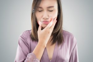 Woman in a silk robe holding her hand to her jaw in pain