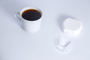 Clear aligners next to cup of coffee on white background