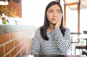 Woman at a café rubbing her jaw because of TMJ pain