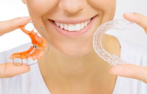 Woman holding retainer along with clear aligner. 